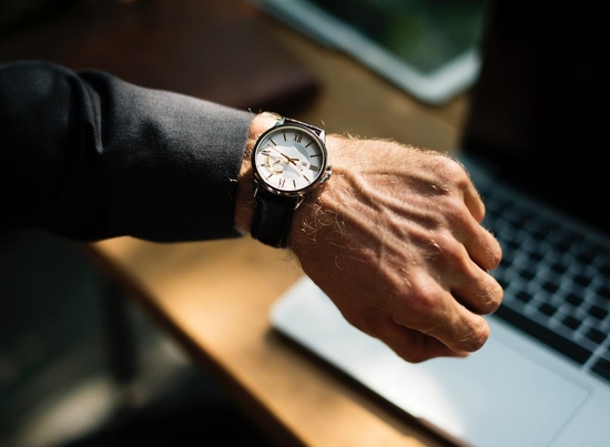 Man wearing wrist watch with leather strap and white clock face.