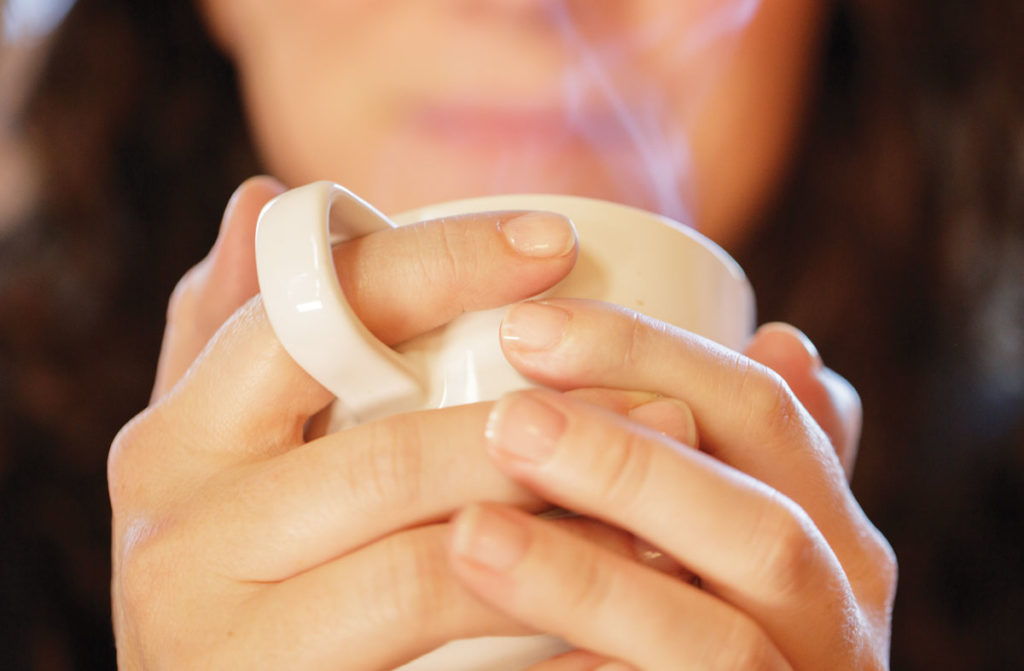 Woman holding white mug of tea inhaling steam from mug