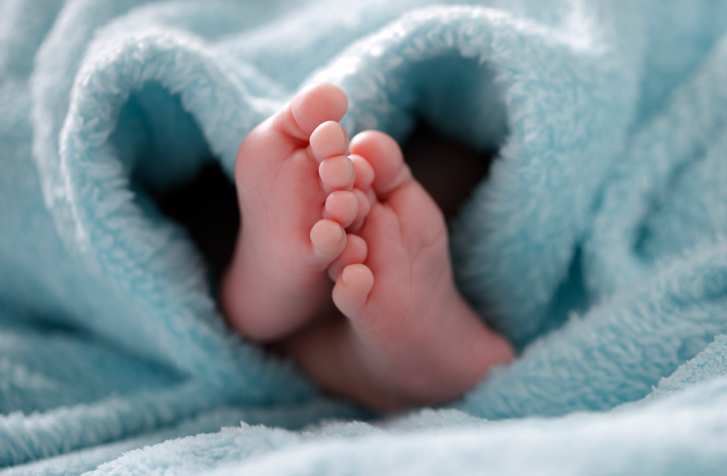 Newborn feet poking out of soft, blue blanket